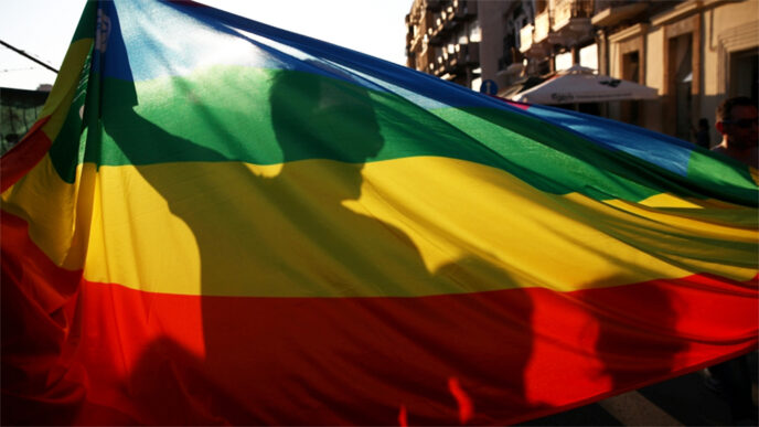 A man in silhouette behind a rainbow Pride flag.