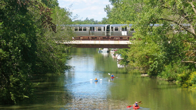 An elevated train crosses the Chicago River while kayakers paddle beneath the rail bridge.