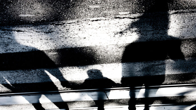 Shadows of two adults and a child holding hands over a crosswalk.